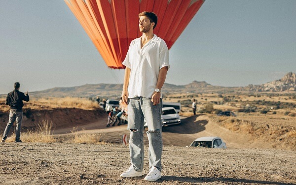 Man wearing a white shirt with ripped jeans and white sneakers.